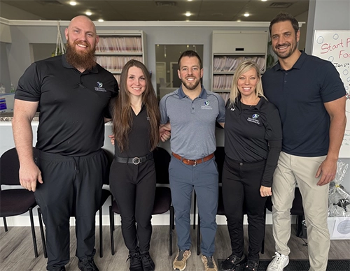Chiropractor Chesterfield MI Eric DiMartino Steven Light Josh Papineau Whitney Pinson Janet Bednarz HP Dr. Josh Papineau D.C., Dr. Whitney Pinson D.C., Dr. Steven Light D.C., Dr. Janet Bednarz D.C., & Dr. Eric DiMartino D.C. smiling in the clinic.